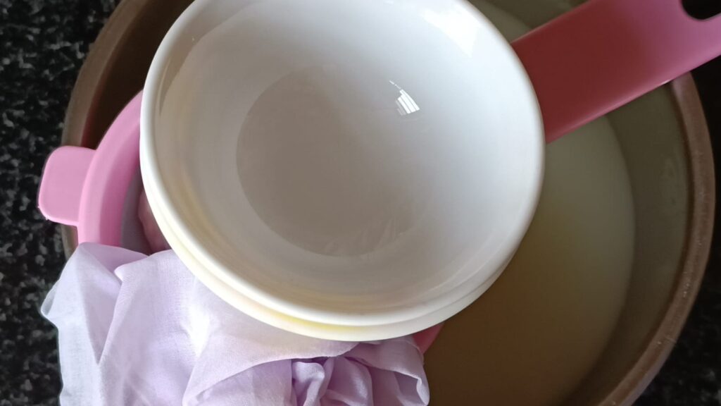 Placing the muslin cloth in a strainer. Some weights put on it to strain the rest of water from paneer to make bengali rasgulla