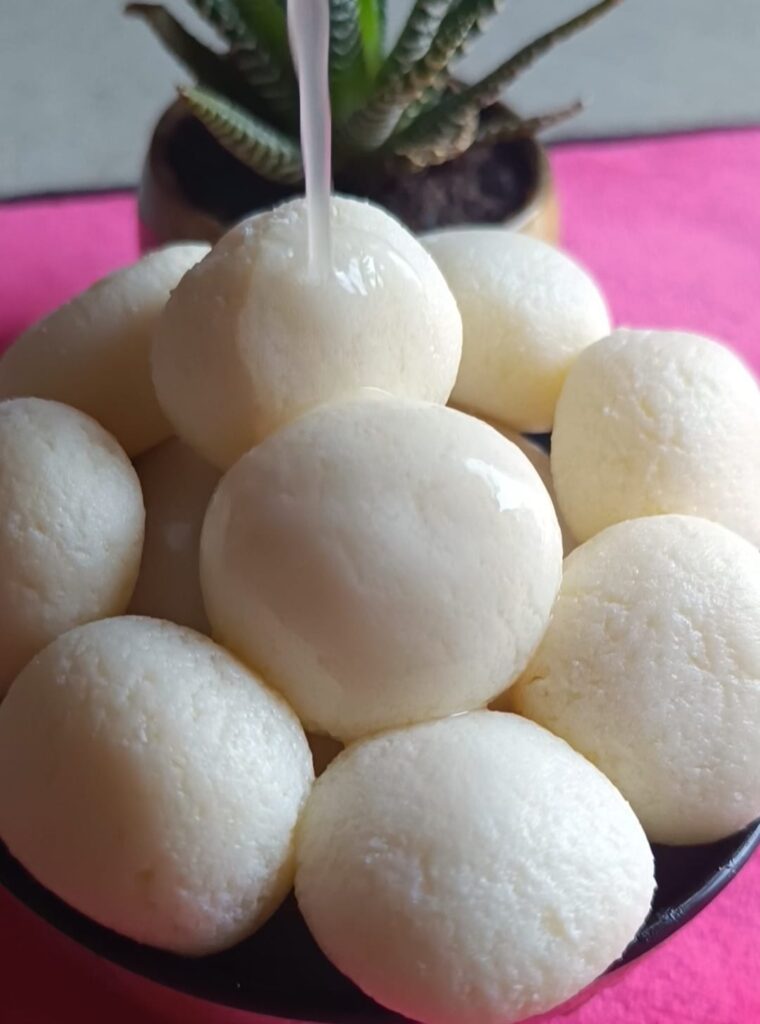 Bengali Rasgullas are now ready to serve. these are kept in a bowl. A small plant is kept near the bowl