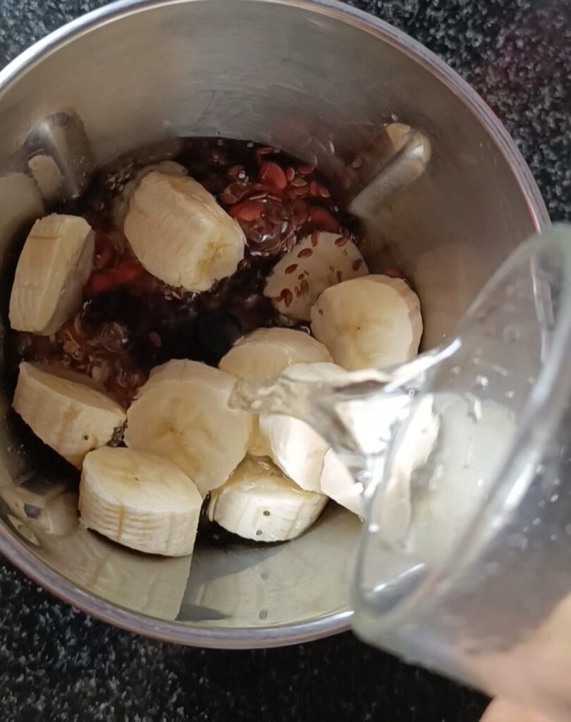 Adding oats, peanuts, dates, chia seeds, flax seeds, banana and water into mixer grinder jar