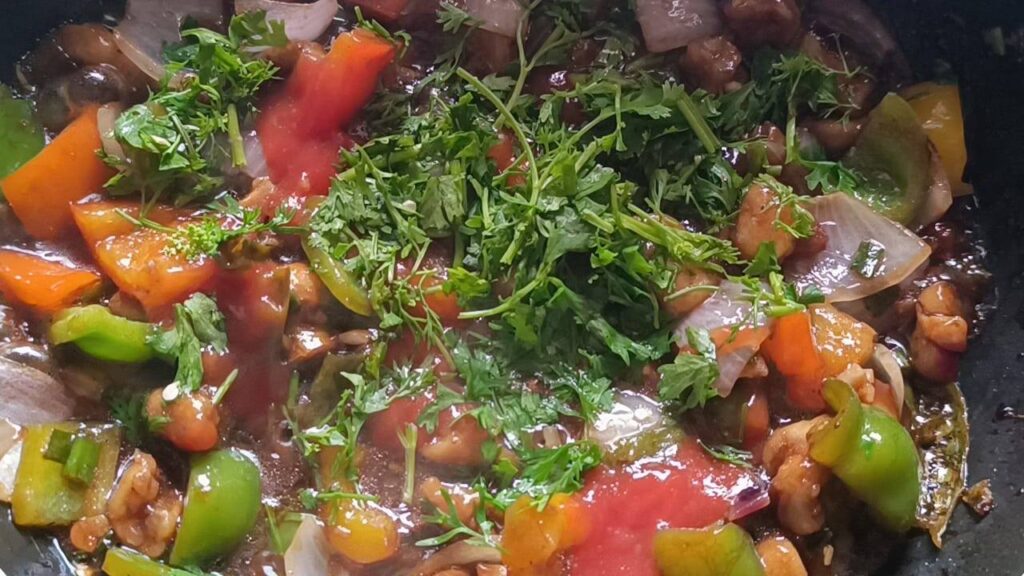 Tomato sauce, coriander leaves are added to the wok with fried mushrooms and other ingredients for chilli mushroom recipe